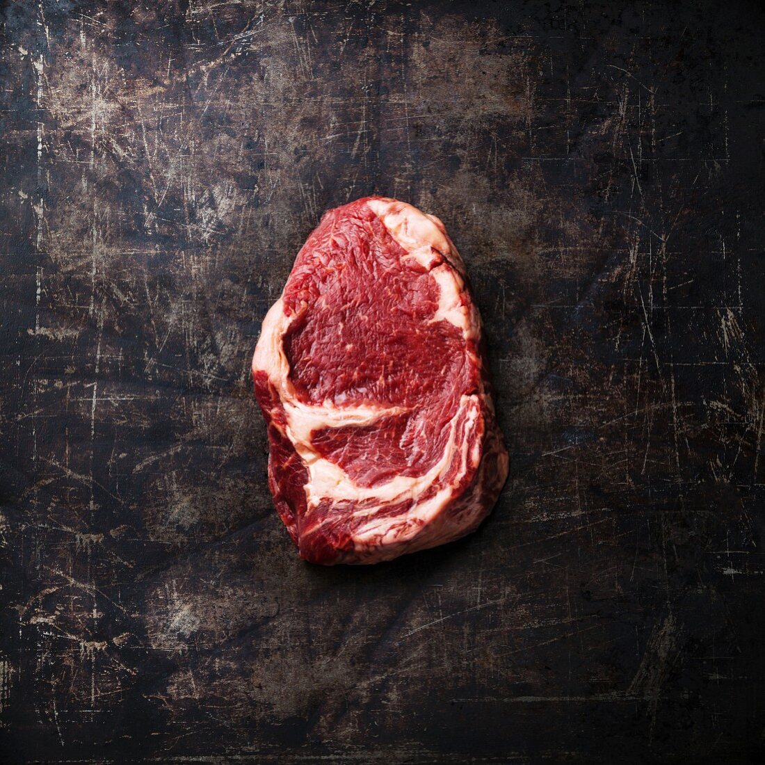Ein rohes Ribeye Steak auf dunklem Metalluntergrund (Aufsicht)