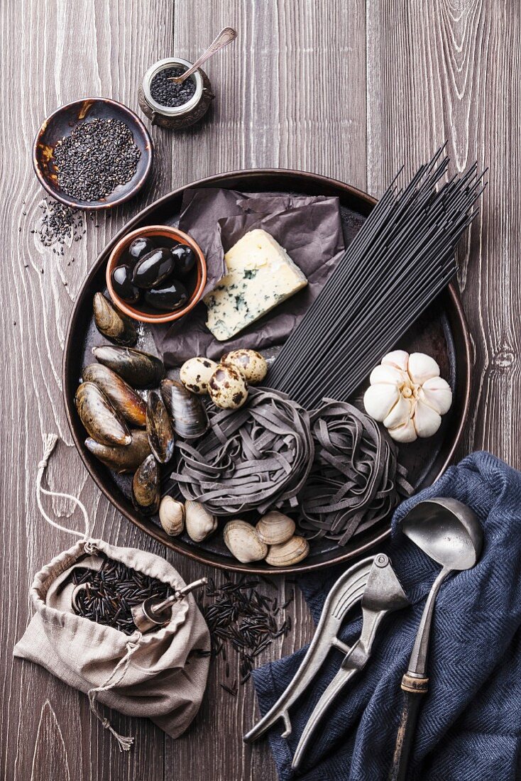 Black raw food ingredients - Pasta, olives, clams on wooden background