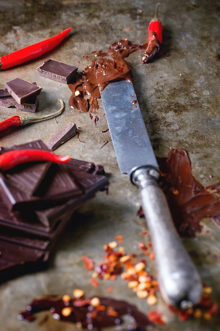 Schokoladenstücke, Messer mit geschmolzener Schokolade und Chilischoten