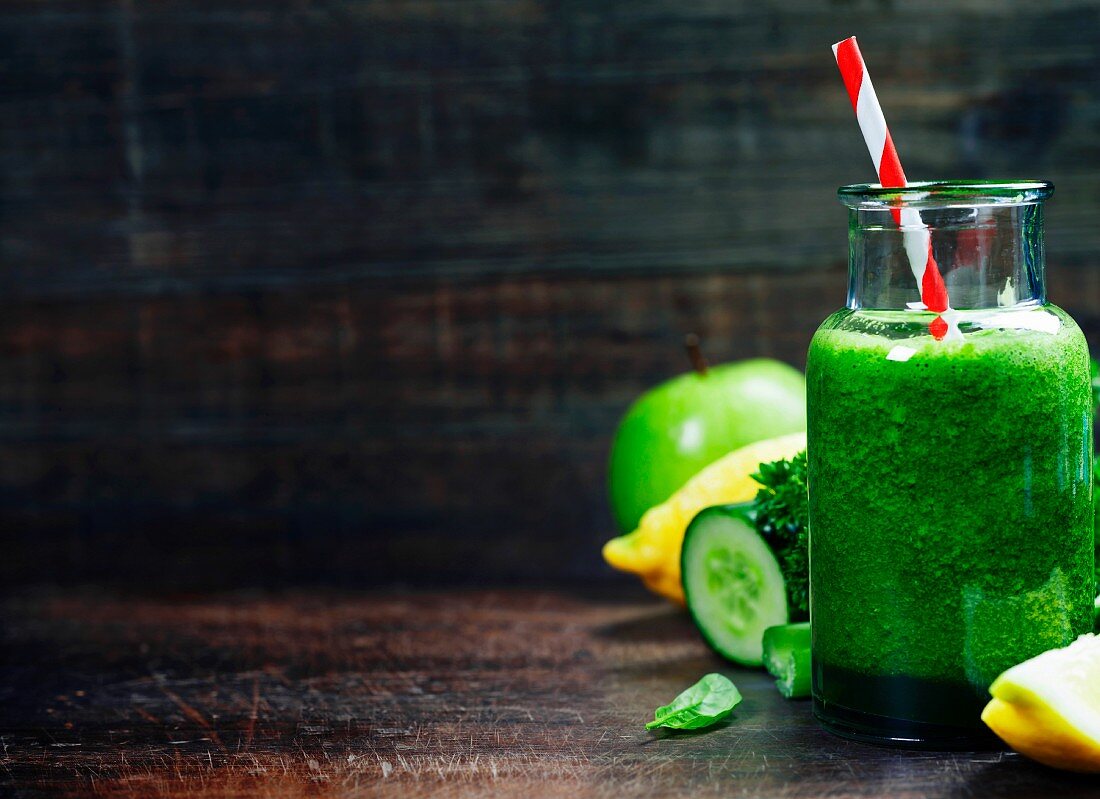 Fresh organic green smoothie with spinach, cucumber, parsley, celery and lemon on wooden background