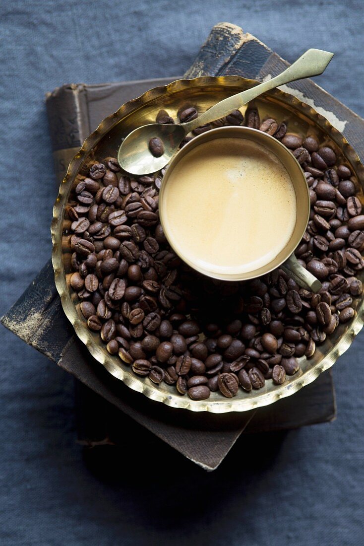 Tasse Kaffee umgeben von Kaffeebohnen auf Metallteller