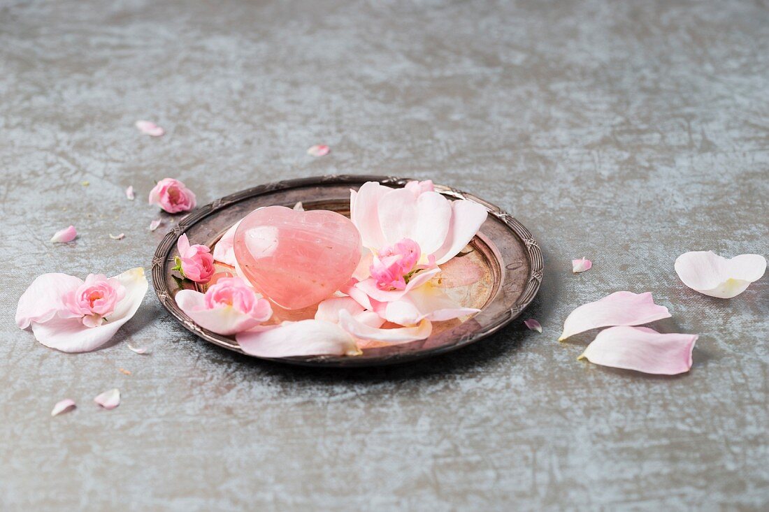 Rosenquarz mit Rosenblütenblättern auf Silberteller