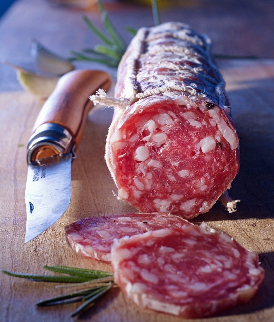 A sliced French salami and an Opinel knife on a wooden board