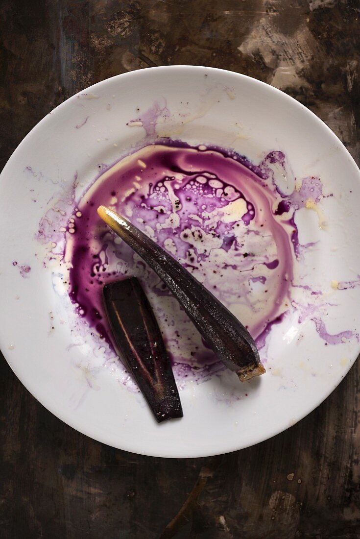 Purple carrot on a white plate with purple juices and oil creating a messy mixture