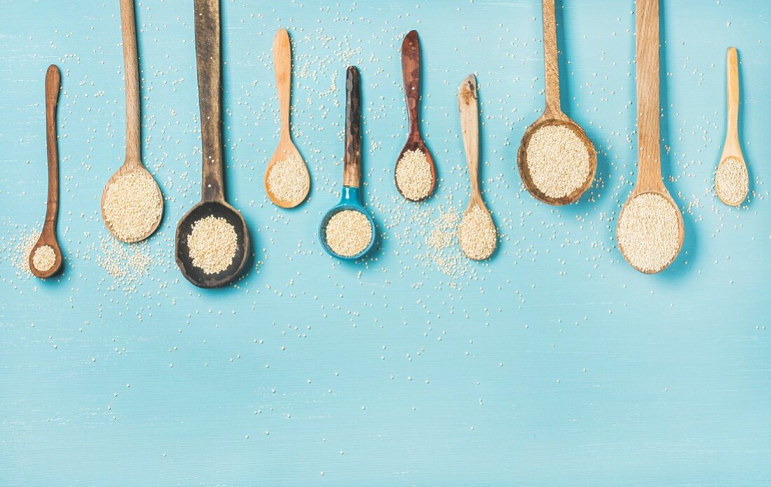 Quinoa seeds in different spoons over blue background
