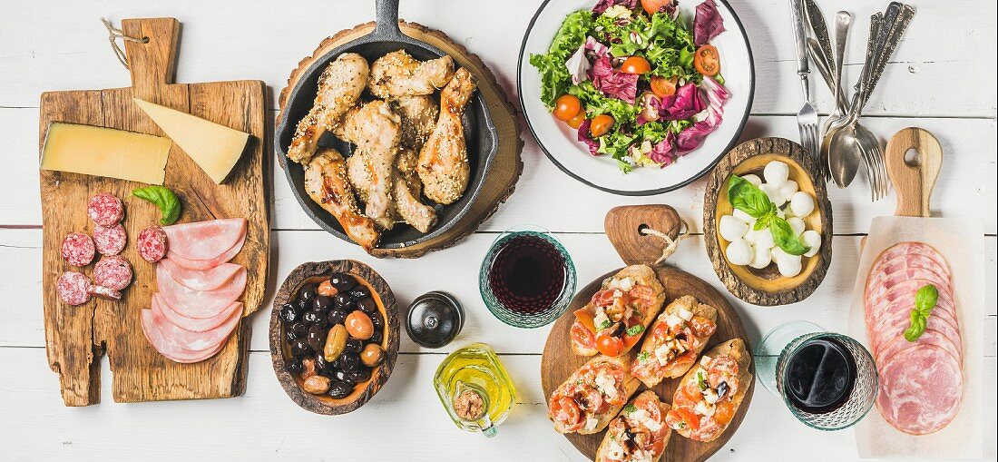 Vorspeisenbuffet mit Hähnchenbeinen, Salat, Oliven, Wurst, Bruschetta und Wein