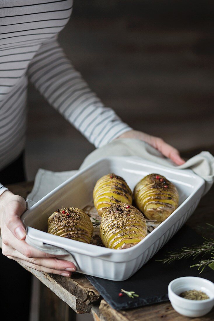 Frau hält Form mit gebackenen Hasselback-Kartoffeln