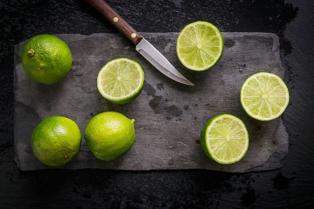 Whole and cut limes on black slate board with vintage knife