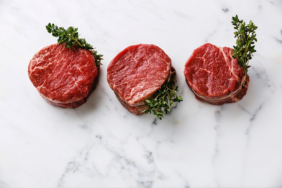 Raw fresh marbled meat Steak filet mignon and thyme on white marble background