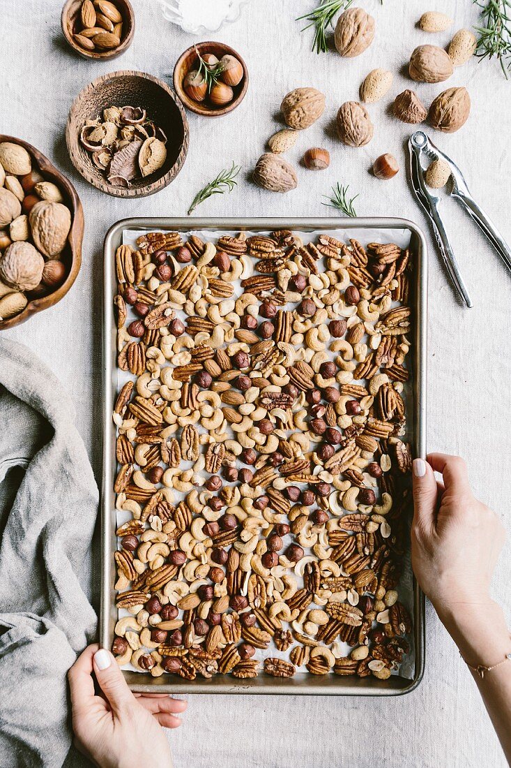 A woman is getting ready to take a sheet full of nuts to toast in the oven