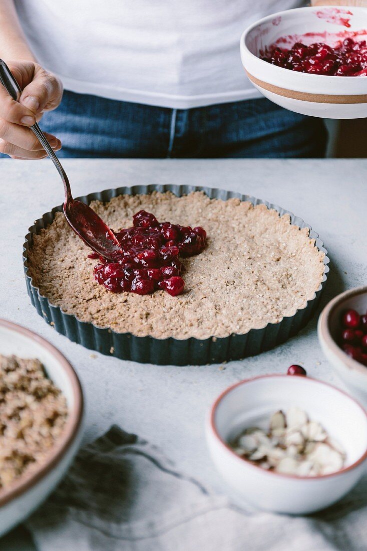 A woman is spreading cranberry sauce on a tart dough