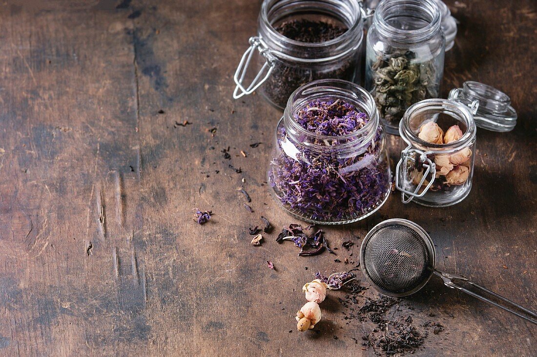 Variety of black, green, rooibos, herbal dry tea leaves and rose buds in glass jars with vintage strainer