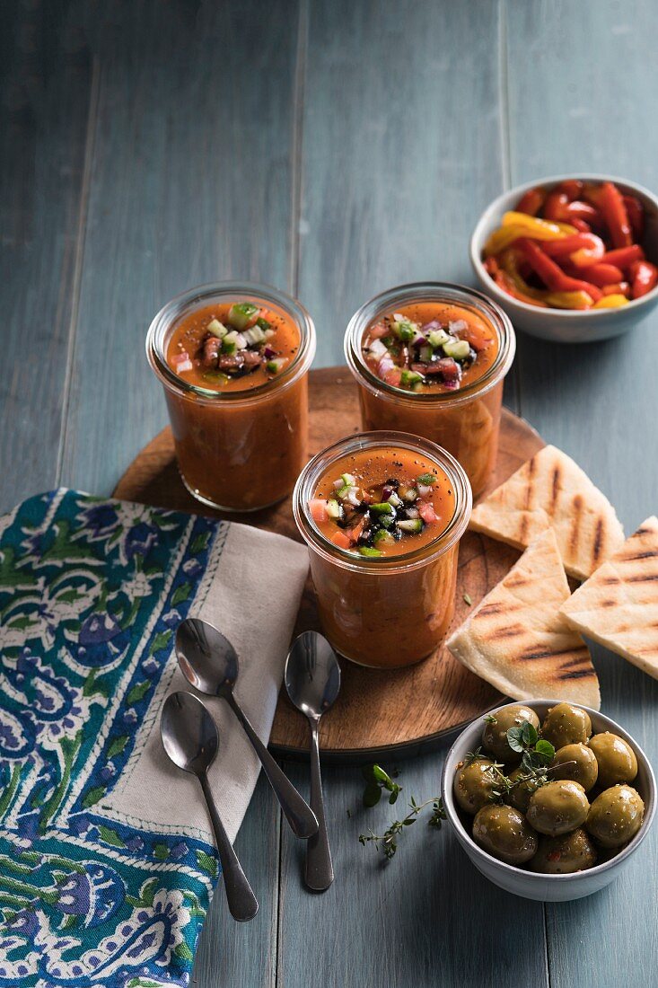 Gazpacho in Gläsern mit gegrilltem Fladenbrot, Oliven und Paprikagemüse