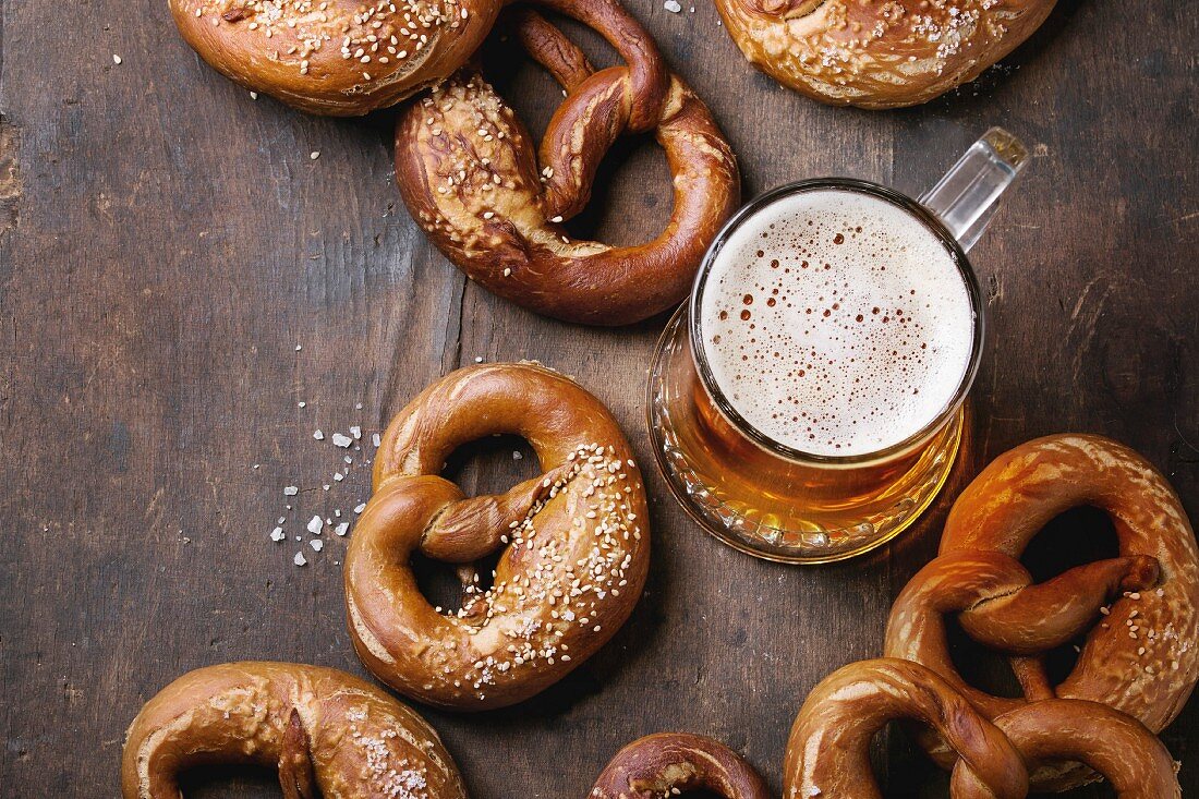 Glass of lager beer with traditional salted pretzels over old dark wooden background