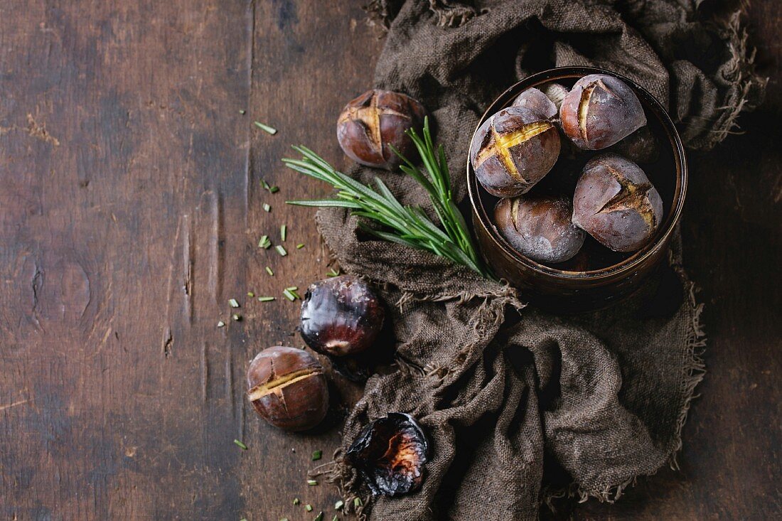 Roasted chestnuts in the ashes with rosemary in tin can on sackcloth over old dark wooden background