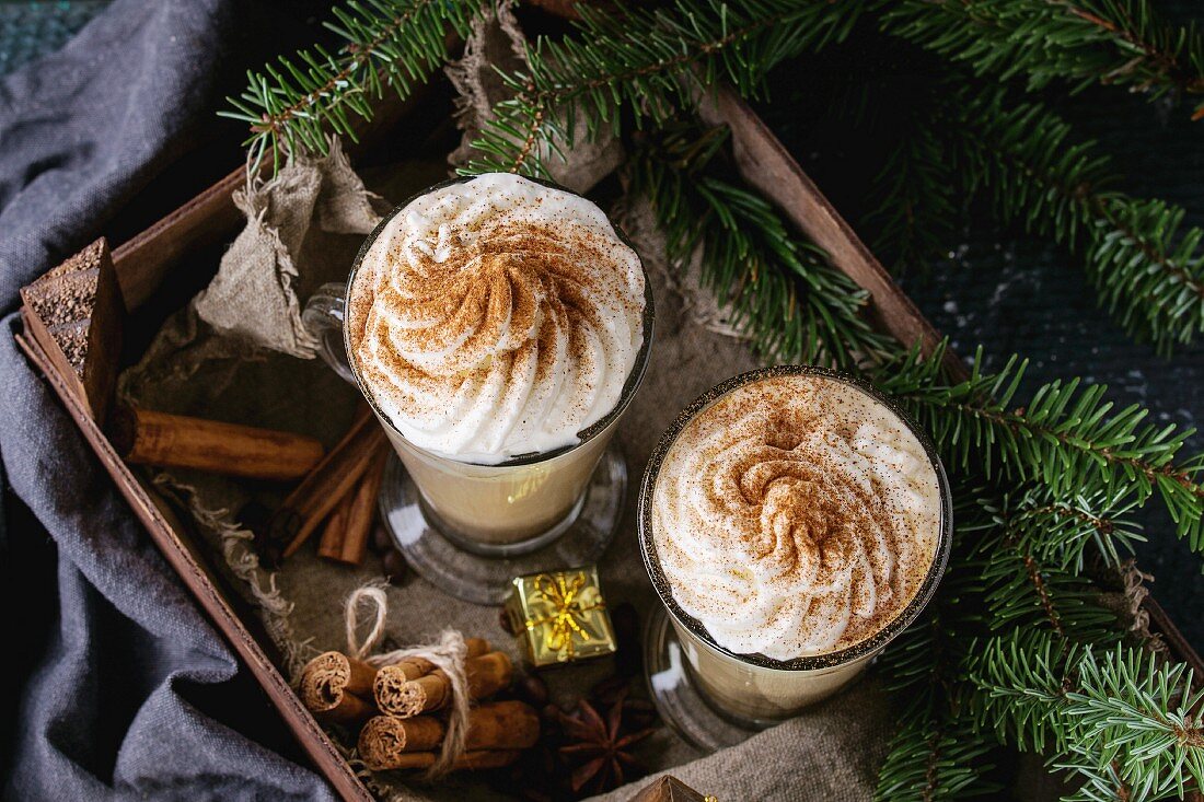 Pumpkin spicy latte with whipped cream and cinnamon in two glasses standing in wooden board with Christmas decoration