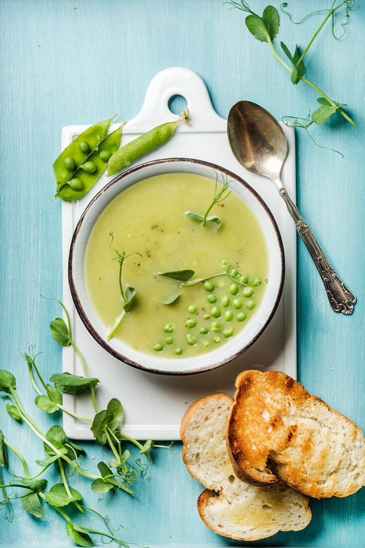 Light summer green pea cream soup in bowl with sprouts, bread toasts and spices