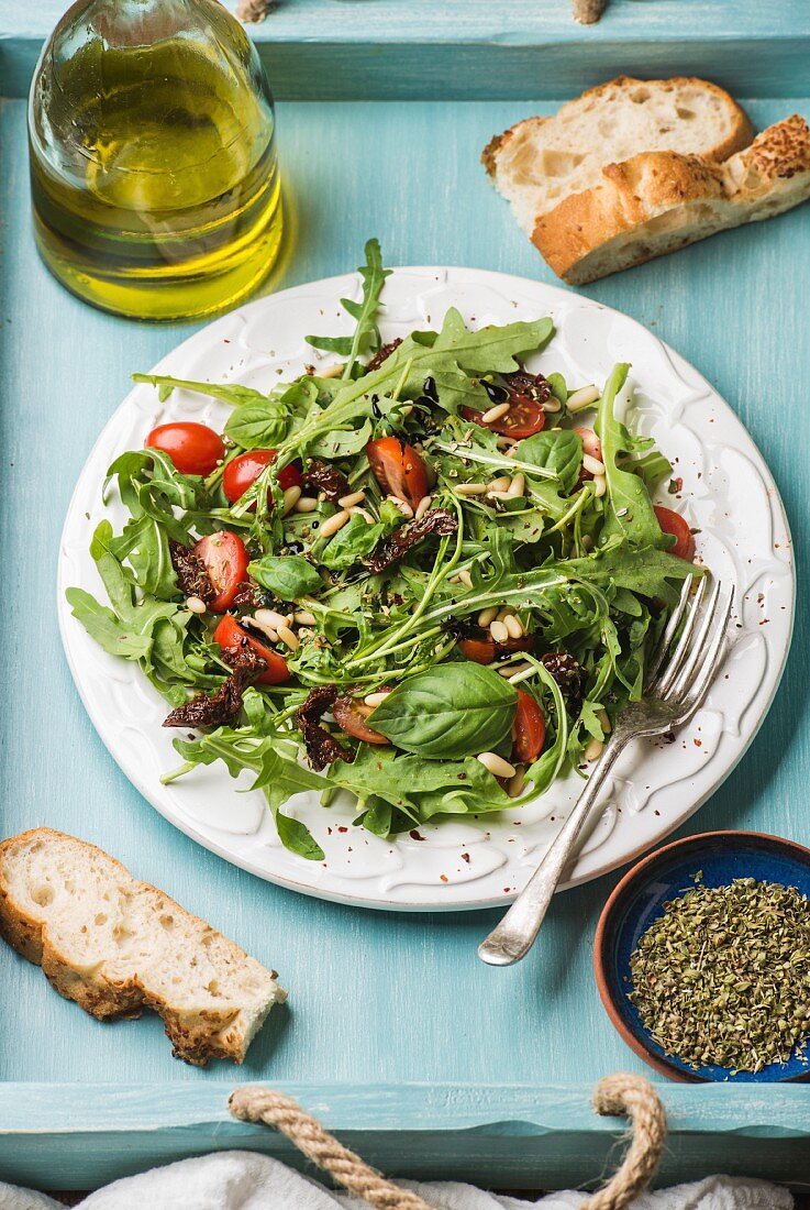 Salad with arugula, cherry tomatoes, pine nuts and herbs on white ceramic plate over blue wood background