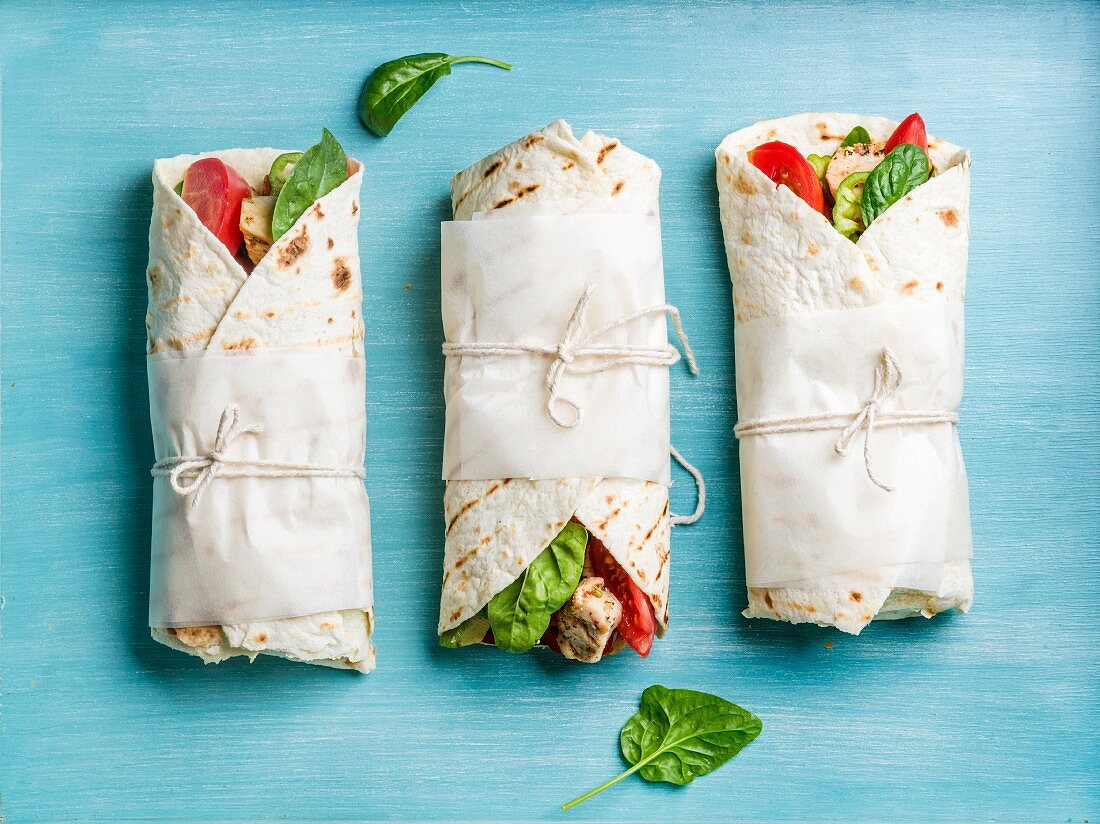 Tortilla wraps with grilled chicken fillet and fresh vegetables on blue painted wooden background