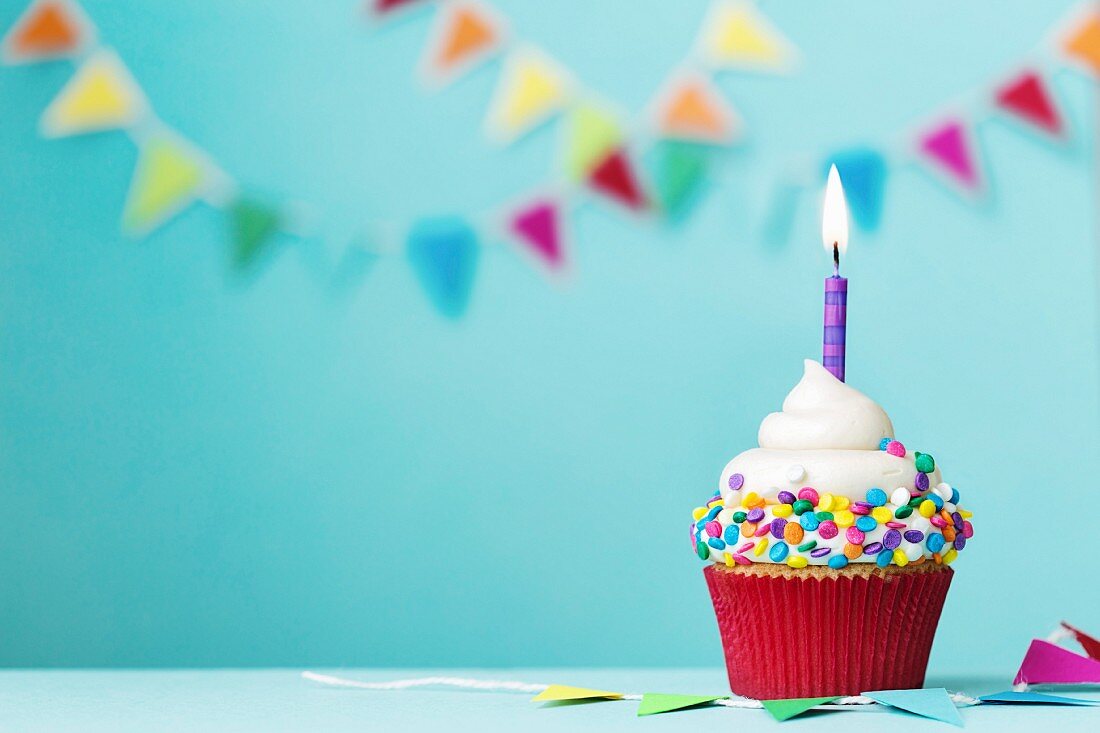 Geburtstags-Cupcake mit brennender Kerze und bunten Zuckerstreuseln
