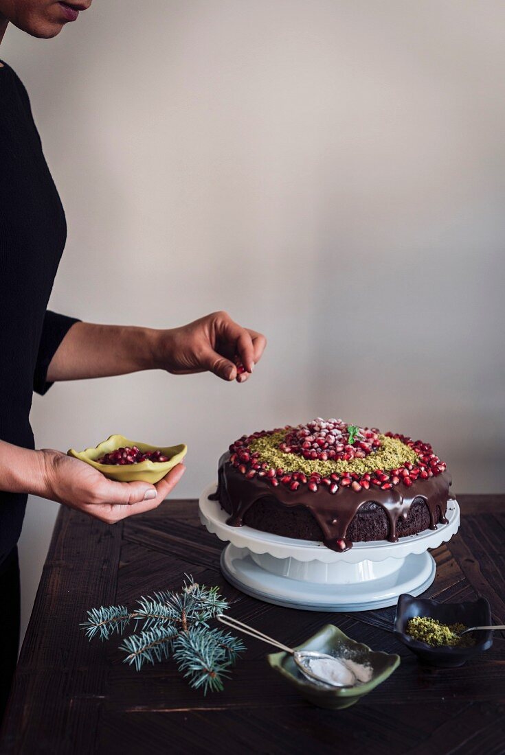 A woman decorating a Christmas Chocolate Cake with pomegranate seeds