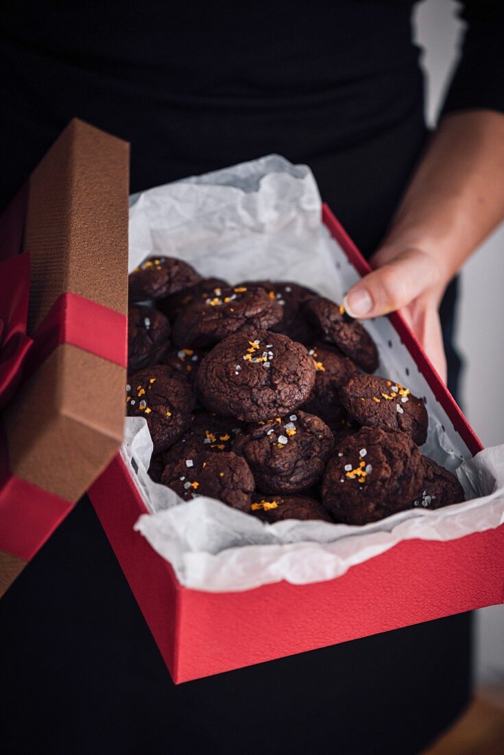 A woman holding a gift box full of chocolate citrus cookies