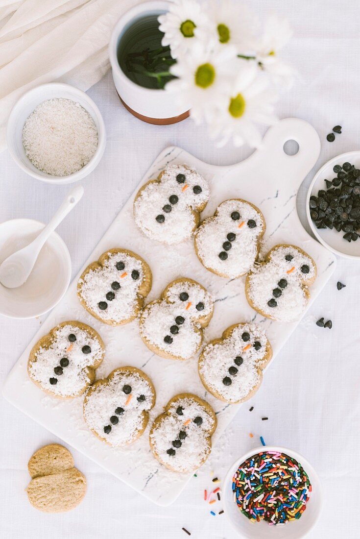 Snowmen cookies with a cute decoration served on a white marble serving board and white flowers aside