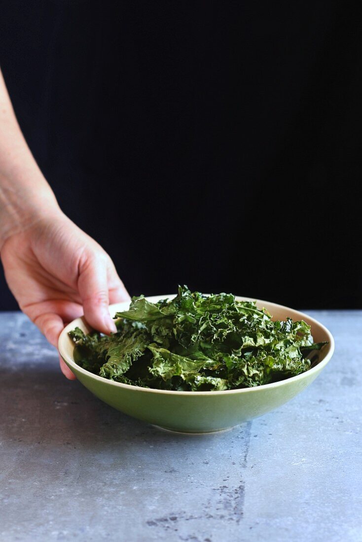Female hand holding a bowl with baked kale chips