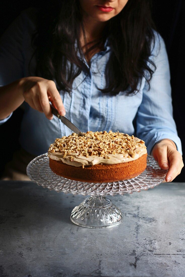 Female cutting a cake topped with cream cheese frosting and walnuts