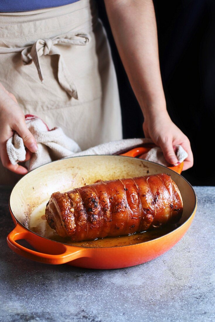 Female hands holding a pan with roasted Italian porchetta
