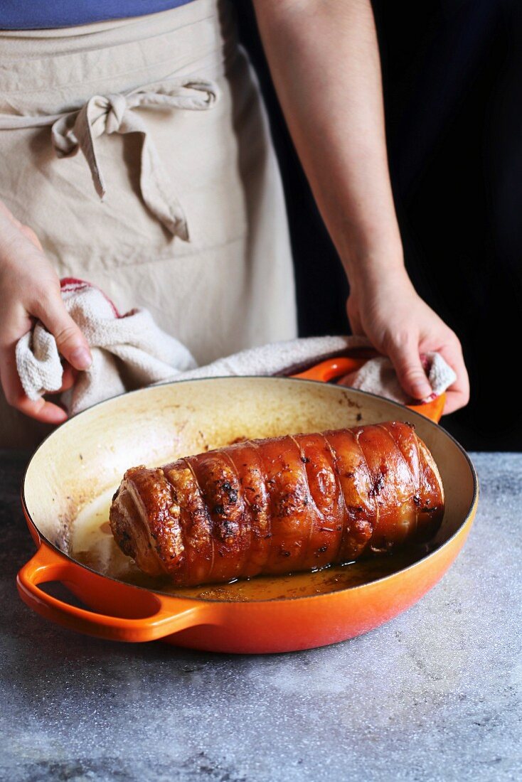 Frau hält Pfanne mit Porchetta (Schweinerollbraten, Italien)