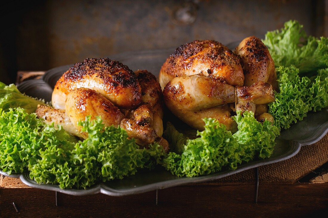 Vintage metal dish with two grilled chicken and green salad over old wooden table