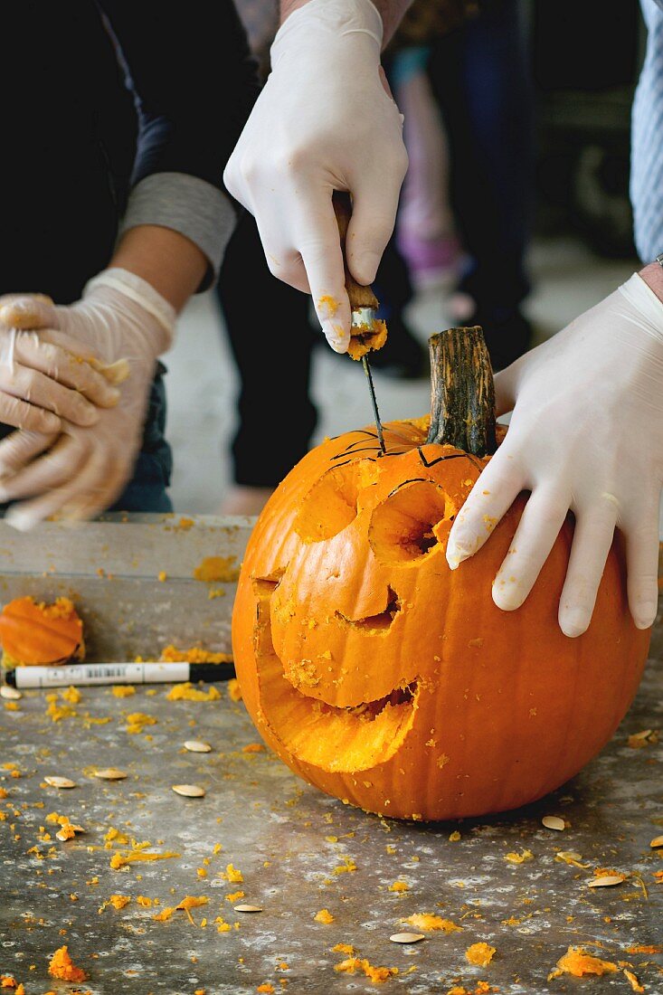 Process of Making Halloween pumpkins, hands in rubber gloves sliced the pumpkin by small hacksaw