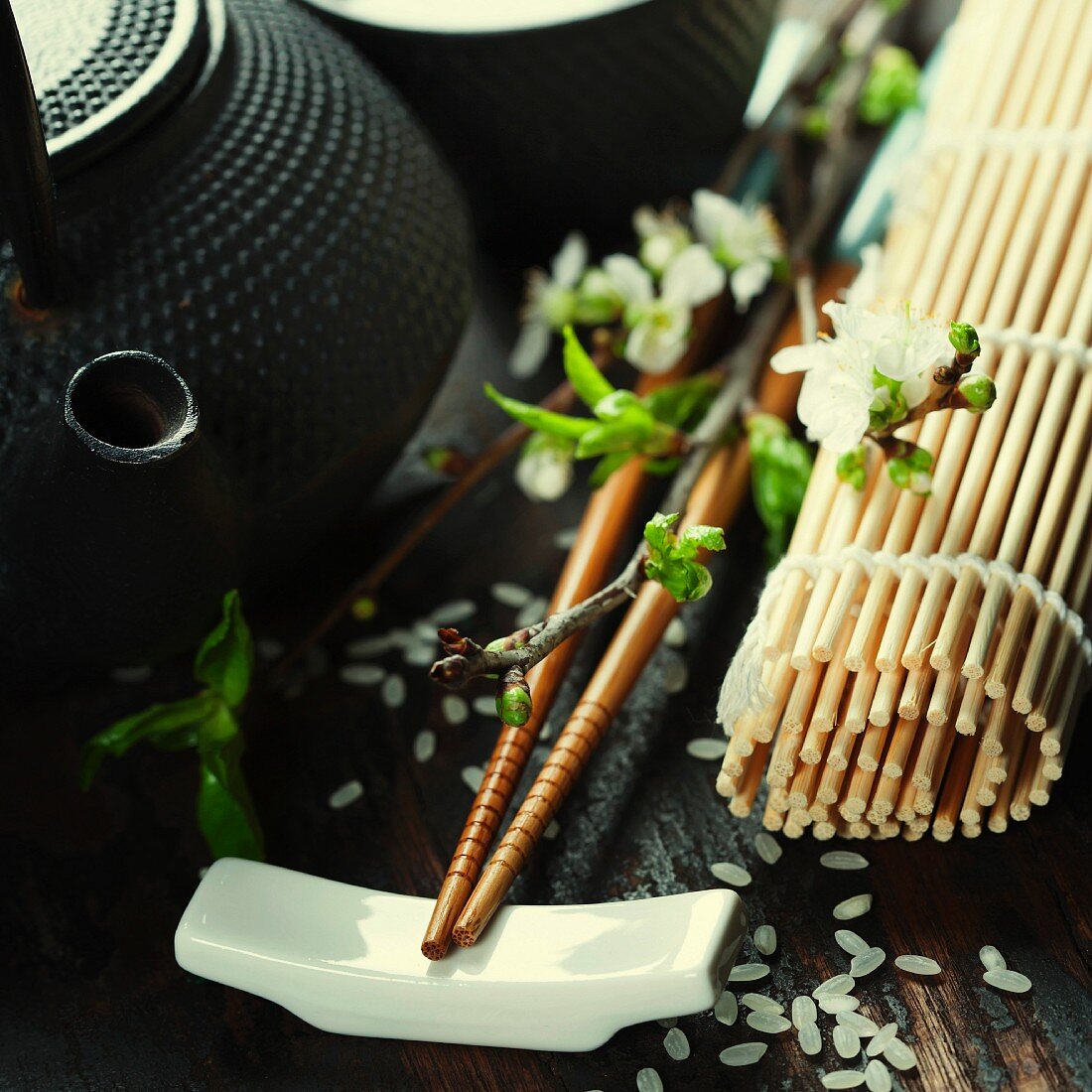 Asiatisches Stillleben mit Teekanne, Essstäbchen, Kirschblütenzweig und Bambusmatte