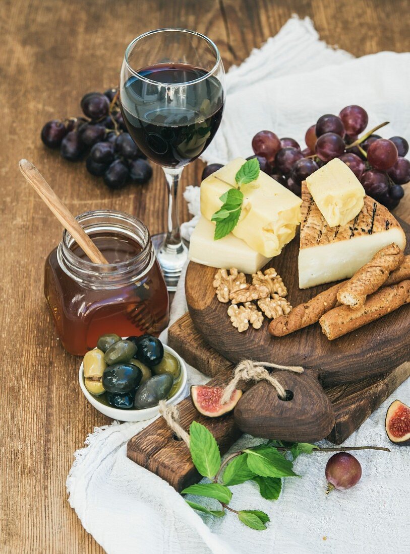 Glass of red wine, cheese board, grapes, fig, strawberries, honey and bread sticks