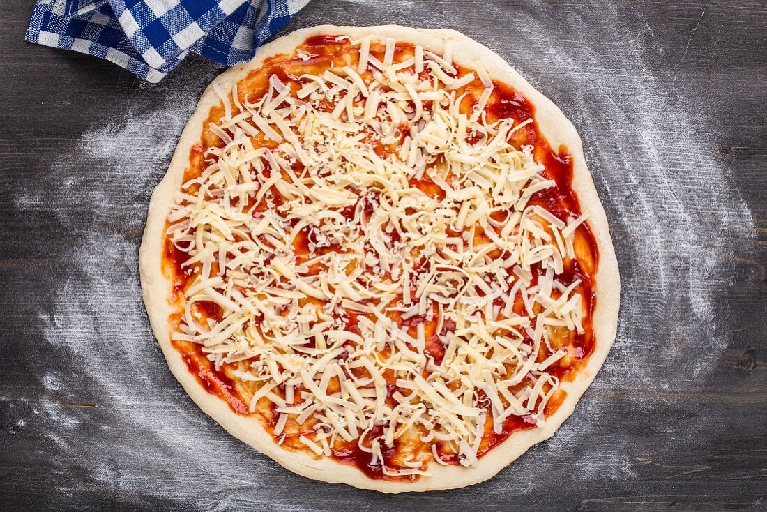 Pizza zubereiten: Pizza mit Käse bestreut (Aufsicht)