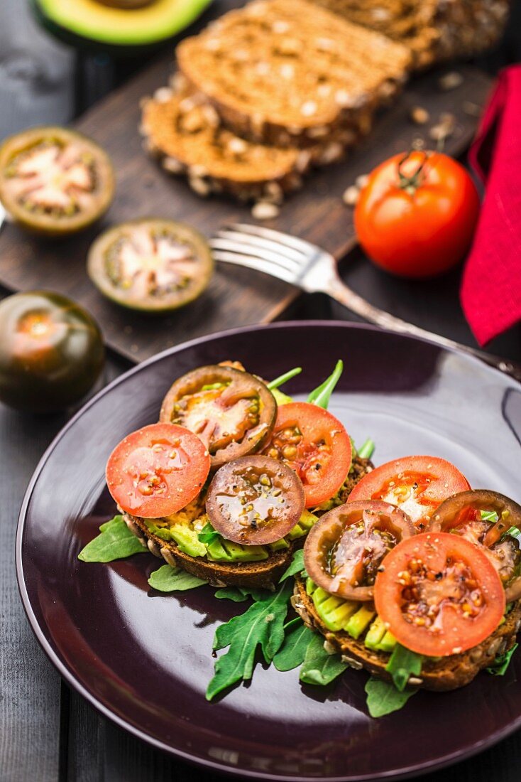 Avocado-Sandwich mit Rucola und Tomaten auf einem Teller