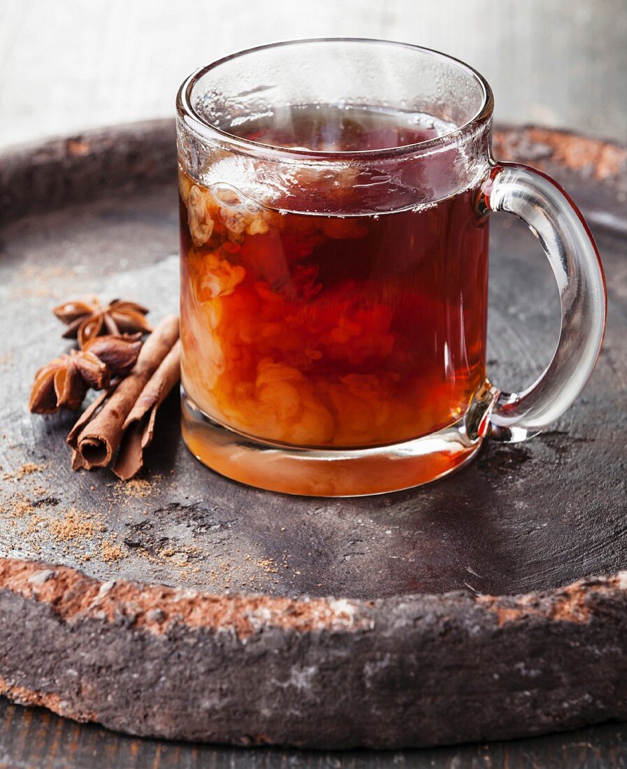 Hot tea with milk and spices on dark background