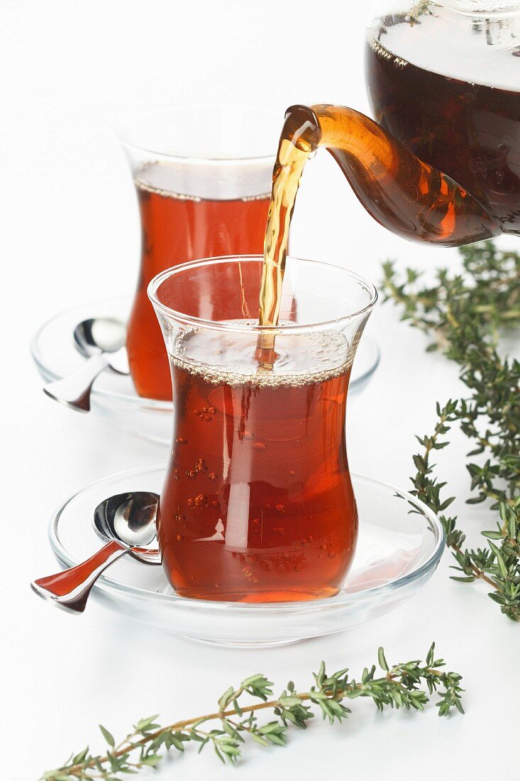 Tea thymus pour into glass cup on white background