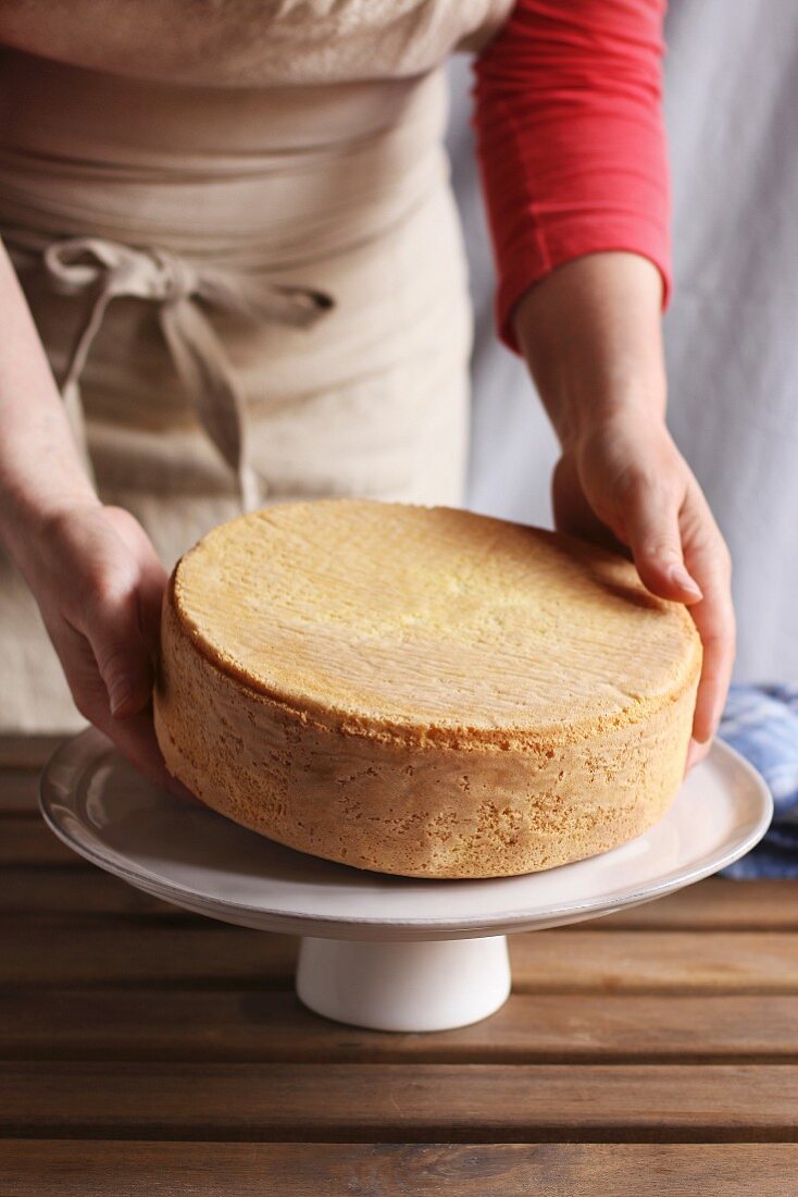 Female hands placing a sponge cake on a cake stand