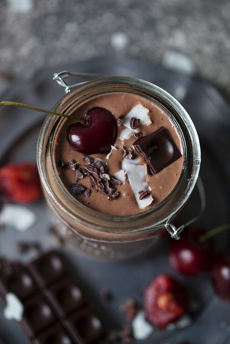 Chocolate coconut smoothie in a jar topped with cherry, dark chocolate, coconut flakes and cacao nibs