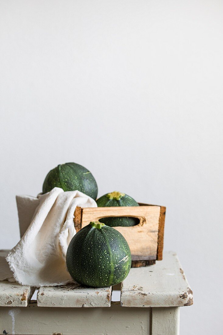 Stillleben mit runden grünen Zucchinis in Holzkiste auf Vintage-Hocker