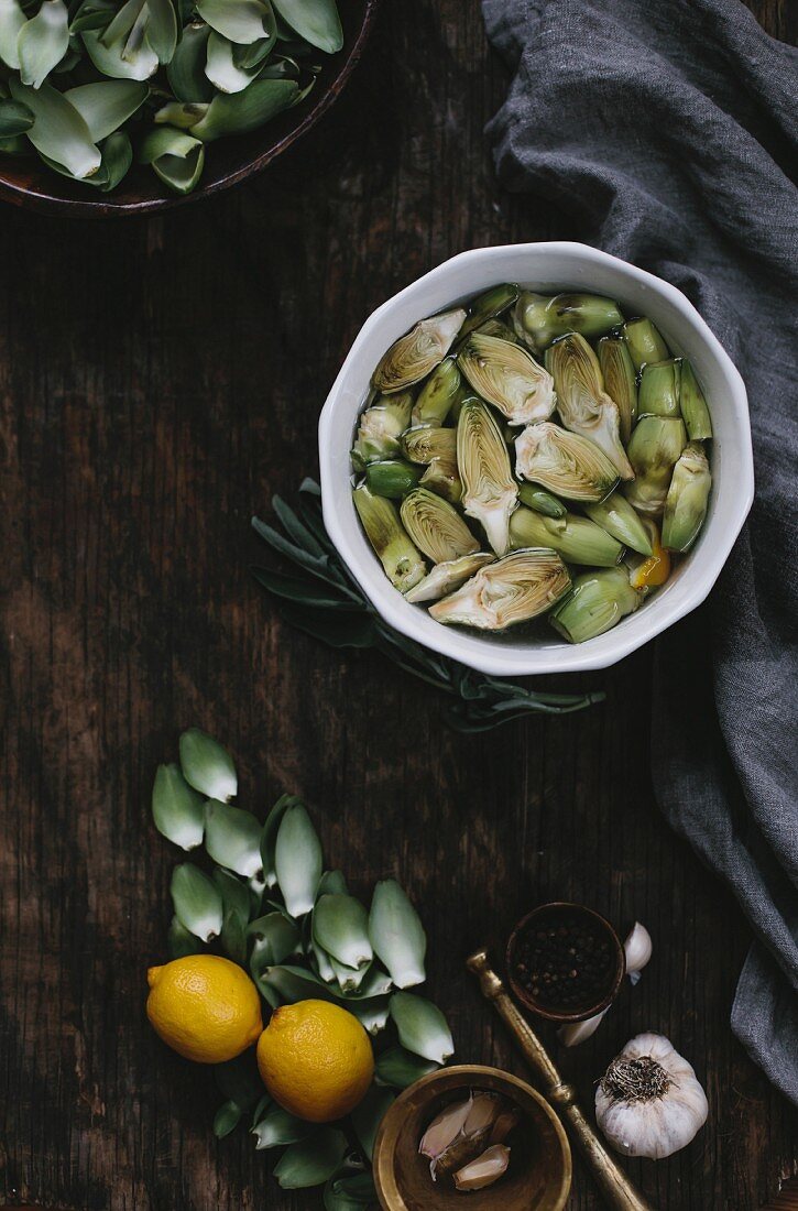 A bowl filled with lemon juice, lemon slices, and peeled baby artichokes