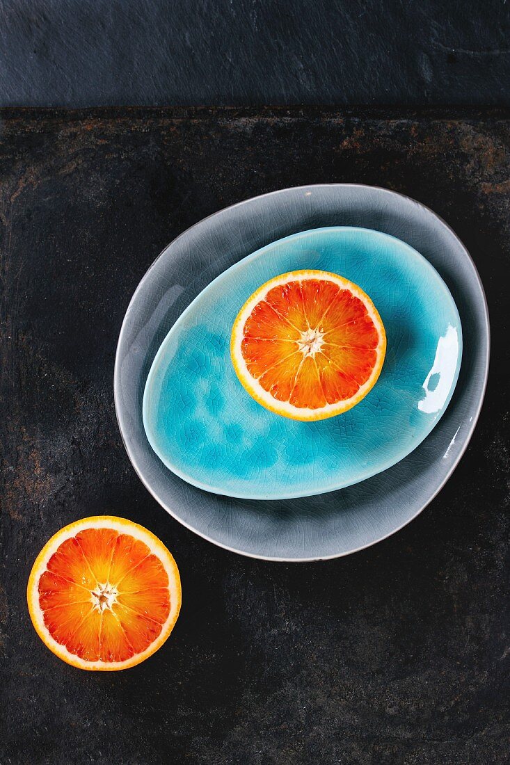 Sliced Sicilian Blood orange fruit on bright turquoise and gray ceramic plates over black background