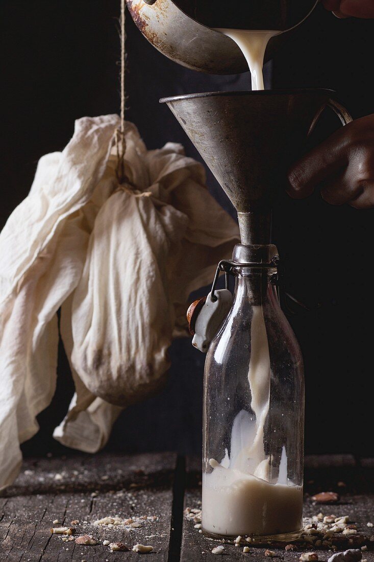 Process of making non-dairy almond milk - woman s hands pouring milk from pan in glass bottle via old funnel