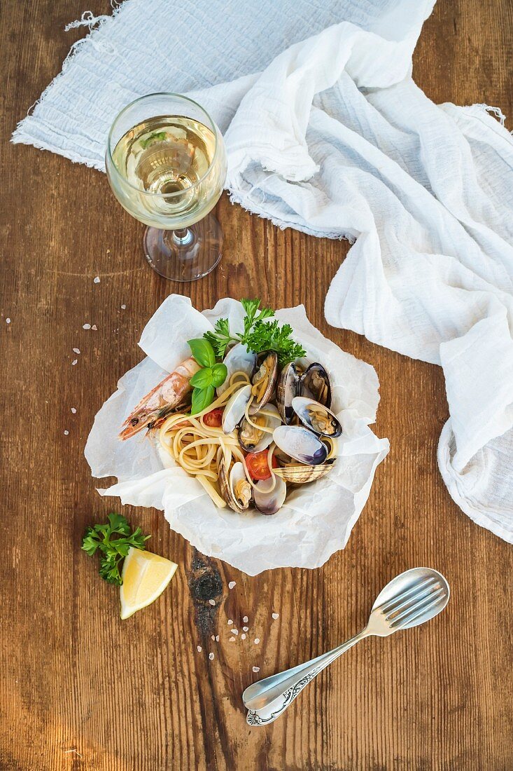 Seafood pasta. Linguine with clams and shrimps in bowl, glass of white wine over rustic wood background