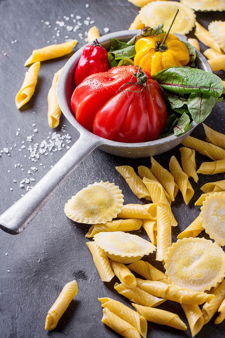 Homemade ravioli and garganelli pasta and vintage colander with tomato RAF, salad leaves and yellow chili pepper