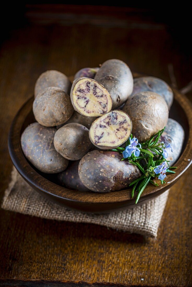 Purple potatoes in a wooden bowl, with one cut open