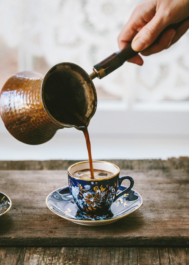 Türkischer Kaffee wird aus Ibrik in Vintage-Kaffeetasse gegossen