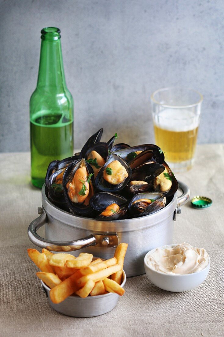 Cooked mussels in an aluminum pan with french fries, mayonnaise and a glass of beer